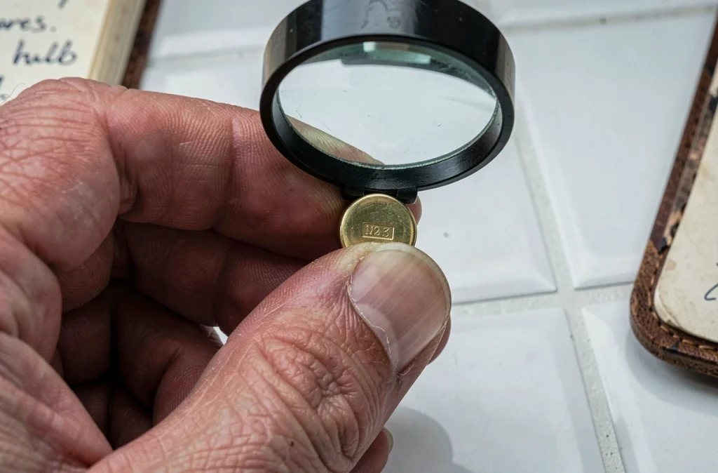 Gros plan d'une main tenant un pendentif en or sous une loupe révélant un poinçon gravé